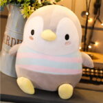 Close-up of a soft, white chubby penguin plushie with a yellow beak and feet. It features pastel stripes and cute facial details.