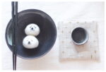 DIY Kawaii Roly Poly Rice Balls kit with two shaped rice balls on a cloth, near chopsticks and a cup.