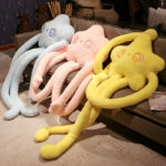 Three long limb plushies – Flowery Stars, in blue, pink, and yellow, displayed on a couch.