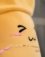 Close-up of a yellow bubble tea plushie with embroidered pink lips and a '7' and 'M'