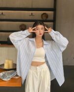 Woman wearing a blue striped Korean aesthetic shirt with white pants.