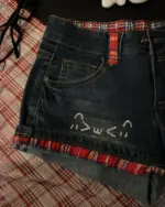 Close-up of kawaii denim shorts with red plaid trim and hand-drawn design.
