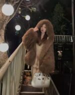 Woman wearing a brown puffy hooded coat outdoors at night.