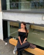 Woman wearing a korean off-shoulder top and black pants, sitting on a wooden bench.
