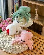 Three spooky cute spider plush toys in green, white, and pink, displayed on a wooden surface.