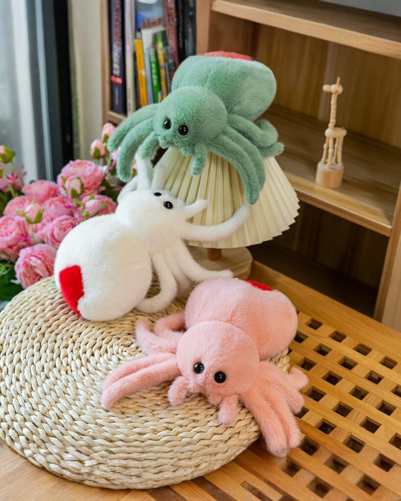 Three spooky cute spider plush toys in green, white, and pink, displayed on a wooden surface.