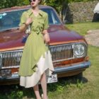 Woman wearing a french vintage dress with a skirt overlay, posing with a vintage car.