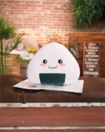 Kawaii onigiri plushie resting on a newspaper, featuring a cute design.