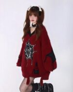 Woman wearing a red loose gothic sweater with spider web details and distressed edges.