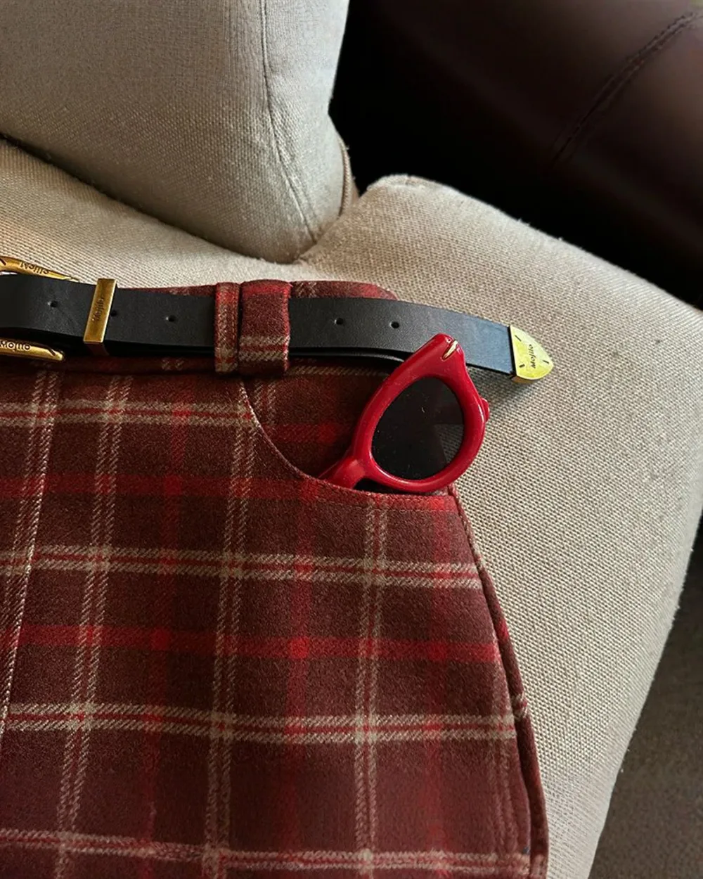 Close-up of a red preppy aesthetic skirt with a plaid pattern and accessories.