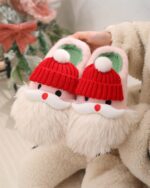 Pair of kawaii santa claus home slippers with hats and pom-poms, cozy winter footwear.