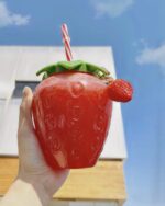 Kawaii strawberry water bottle held outdoors with a straw.
