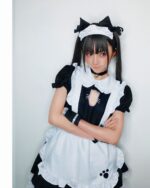 A person wearing a black and white cat maid cosplay costume with a cat ear headband and apron.