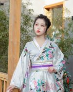 Woman wearing a short floral kimono with peony and bird motifs in a Japanese aesthetic.