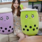 Two cute bubble tea plushies in purple and green, resembling drink containers with boba.