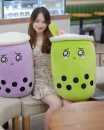 Two cute bubble tea plushies in purple and green, resembling drink containers with boba.