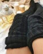 Knitxi knitted thigh high socks in a textured black knit, styled with candles.