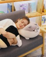 A gray and white super fat shiba plushie resting on a couch.