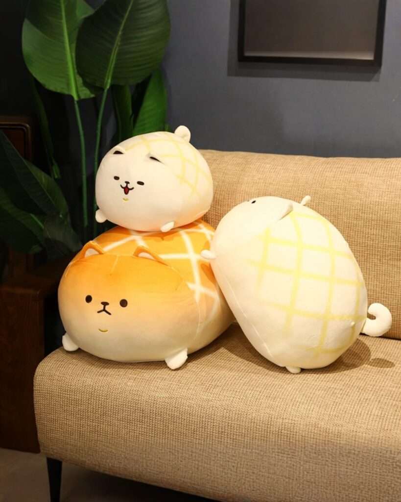 Two kawaii melonwan dog plushies, one orange and one yellow plaid, resting on a couch.