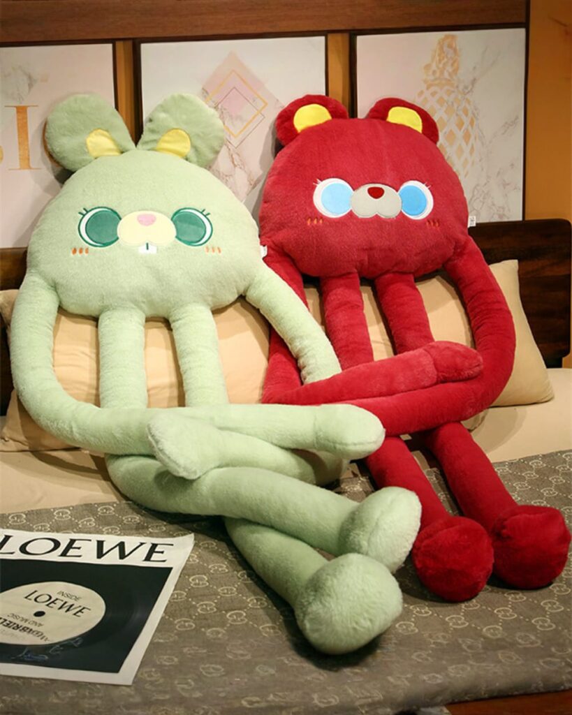 Kawaii long-legged bear plushie and rabbit plush toys, green and red, displayed on a bed.