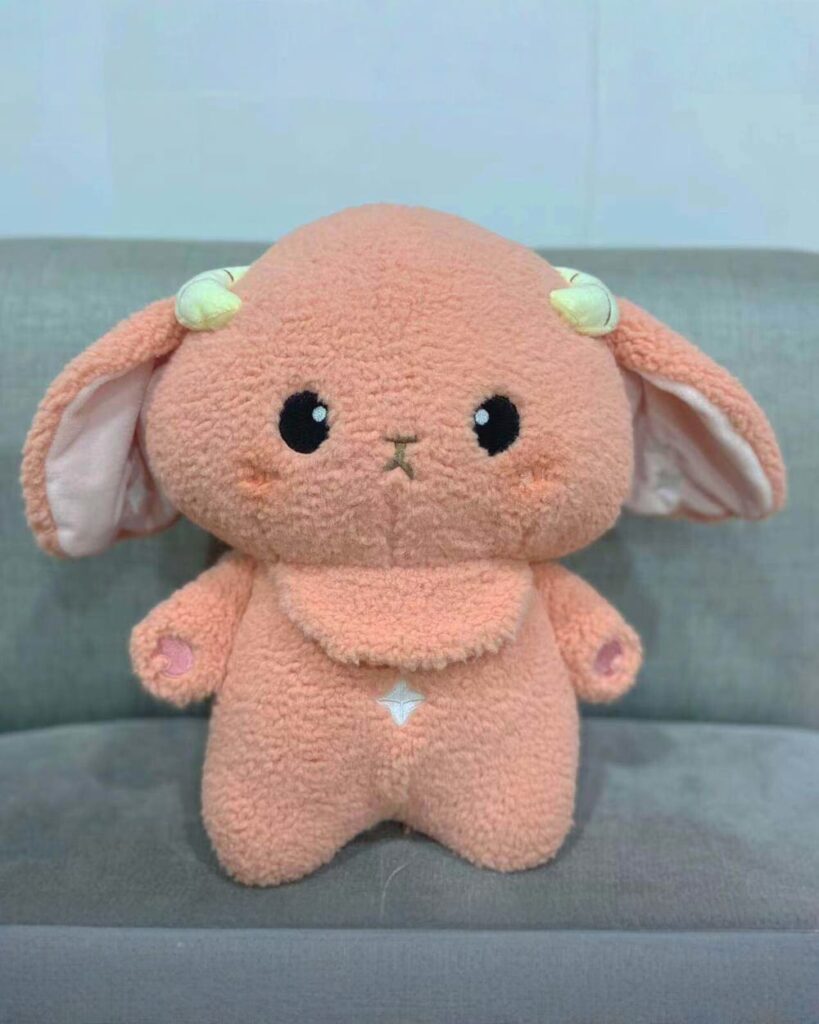 A plush toy, kawaii space sheep plushie, featuring soft pink fur and golden horns.
