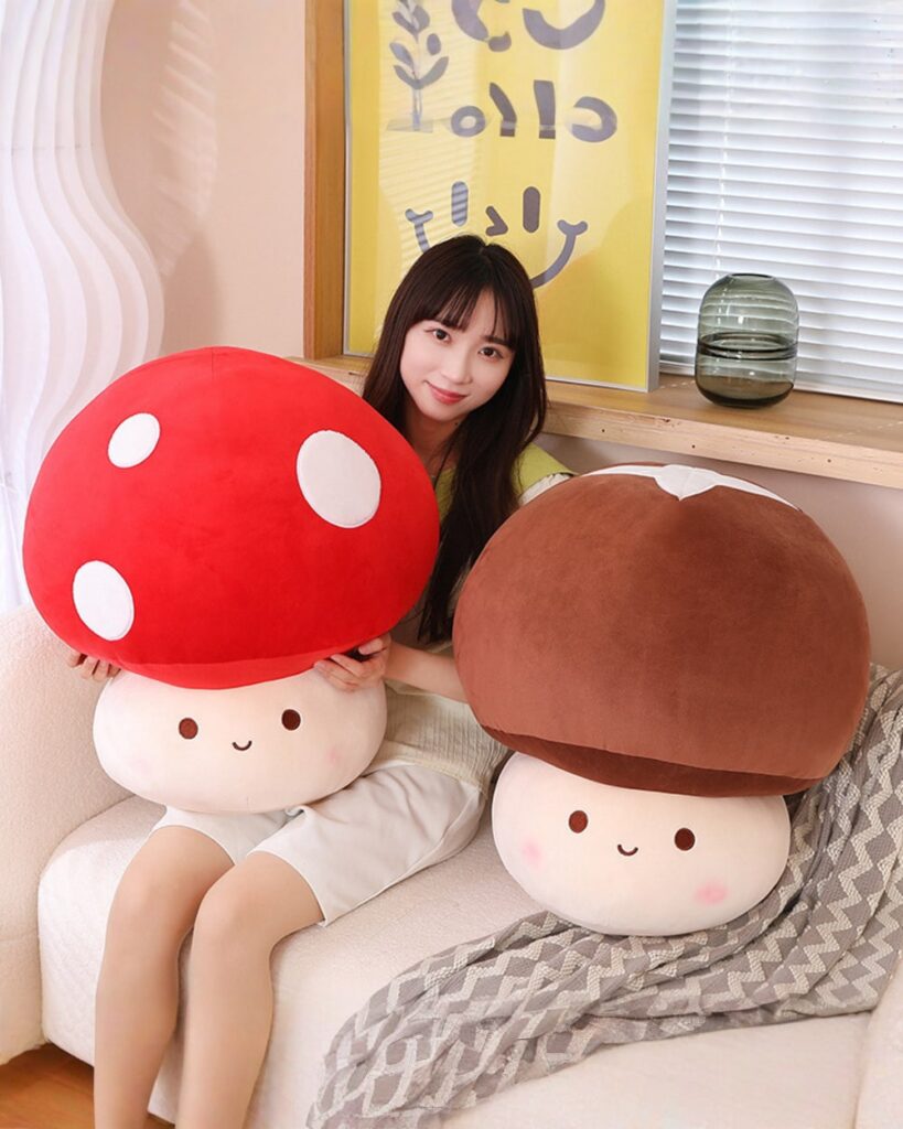 Two giant mushroom plushies, chonky plush toys in red and brown, with smiling faces.