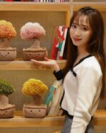 Two plush potted trees - Pachira Edition, displayed on a shelf with a person.