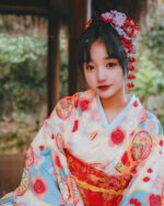 Pink new year kimono featuring a floral print, worn by a woman with traditional Japanese hair accessories.