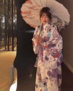 Woman wearing a light purple yukata with floral and bird pattern, holding a parasol.