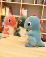 Pink and blue kawaii dino plushie toys displayed on a wooden surface, aesthetic room decor.