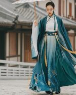 A woman wearing an embroidered jade hanfu, a traditional Chinese garment, outdoors.