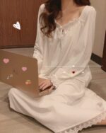 Woman wearing a white soft girl aesthetic nightdress, using a laptop.