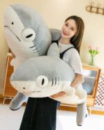 A large gray giant shark plushie, Fins the Chonky Shark, being held by a person.