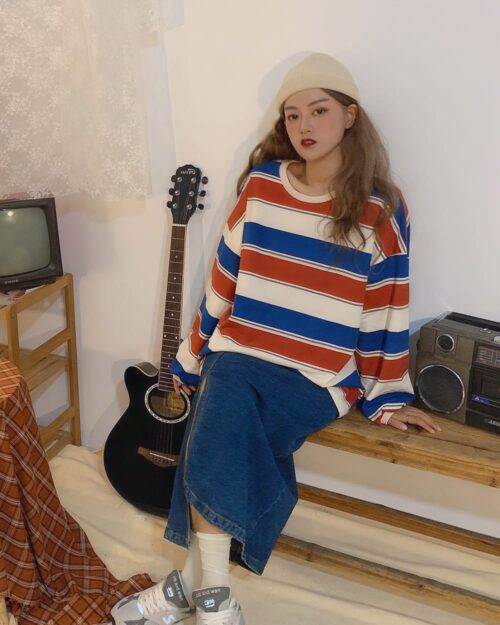 A person wearing a loose striped aesthetic sweatshirt with blue wide-leg pants and sneakers.