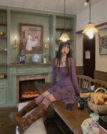 Woman wearing a purple lace gothic aesthetic dress, boots, and glasses in a vintage interior.