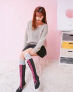 Woman wearing kawaii chicken legs socks, knee-high socks with grey and pink chicken leg design.