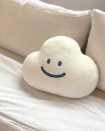 Kawaii happy cloud plushie resting on a white bed. It features a smiling face and soft, fluffy texture.