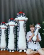 Several long cat plushies, including Whiskers the Stripped Emperor Cat, are displayed with a person.
