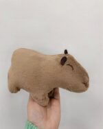 A tan capybara plushie, soft and cuddly, held in hand.