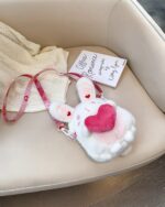 White chibi loli handbag with pink heart details, resting on a sweater and book.