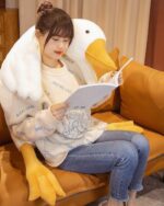 A woman reading with Feather Gang - The Giant Goose Plush in a cozy setting.