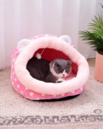 A pink and white kawaii cat bed with plush interior, featuring cat ear details. A gray cat is resting inside.