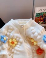 Close-up of a white handmade aesthetic cardigan with floral and pom-pom embellishments.
