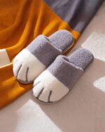 Pair of cat paw slippers featuring a cream and gray faux fur design with a blue sole.