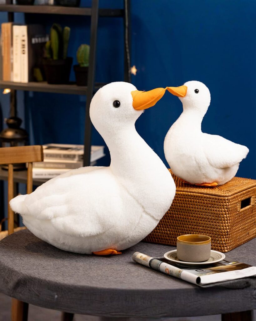Two white duck plushies cuddle together on a table.