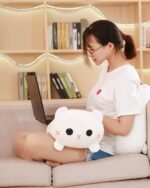 Kawaii milk cat plushie resting on a sofa with a laptop.