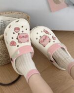 Close-up of pink and white piggy crocs with pig and heart embellishments. Cute piggy crocs footwear.