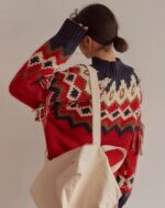 Back view of a red and navy kawaii winter sweater with a patterned knit and fringe detail, held by a person.