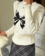 White Korean aesthetic sweater featuring a large black bow print. Casual knitwear with a button closure.