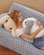 Two big bunny plushies, one grey and one beige, are held by a person.